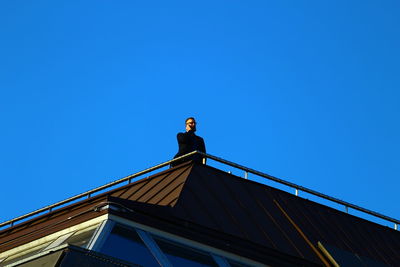 Low angle view of woman standing on roof against clear blue sky