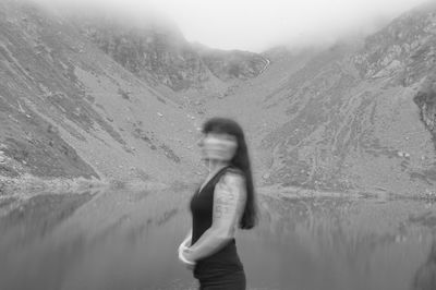 Blurred motion of woman by calm lake against mountain