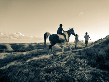 People riding horses on field against sky