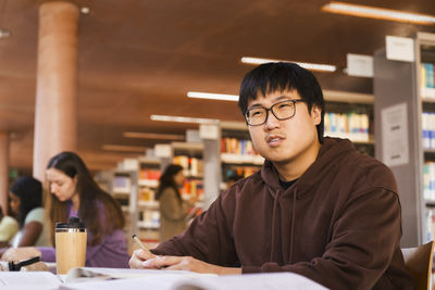 Thoughtful young male university student with books sitting at library desk