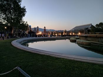 River by illuminated city against clear sky at dusk