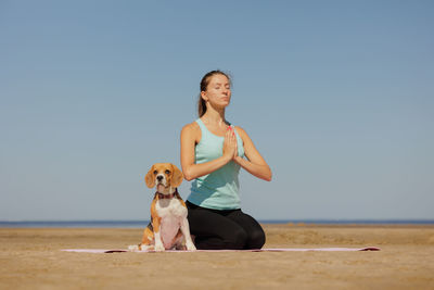 Portrait of young woman with dog on beach against clear sky