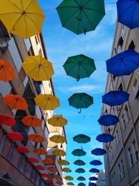 Low angle view of multi colored umbrellas hanging amidst buildings in city