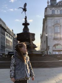 Girl looking away while standing on street in city