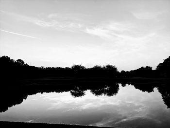 Reflection of silhouette trees in lake against sky