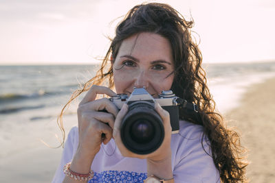 Young woman holding camera at beach