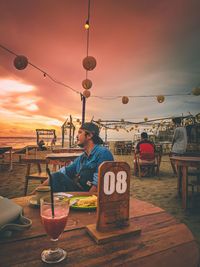 Man sitting at restaurant table against sky during sunset