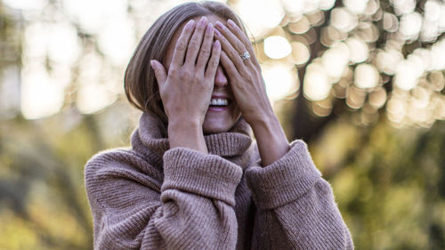 Smiling woman covering eyes at park