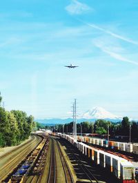 Airplane flying over railroad tracks against sky