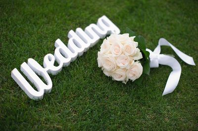 High angle view of white wedding text and bouquet on field