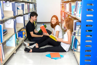 High angle view of happy friends studying while sitting on floor in library