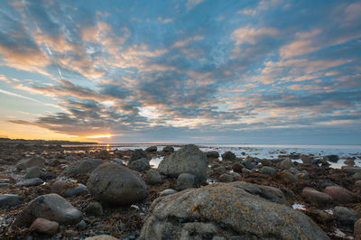 Rocks by sea against sky during sunset