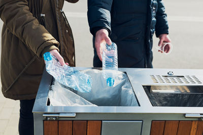 Midsection of people throwing bottles in garbage bin