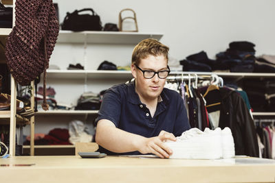 Cashier holding shoes on table while calculating in clothing store