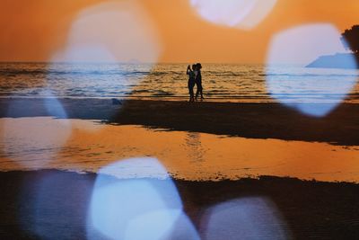 Silhouette people on beach against sky during sunset