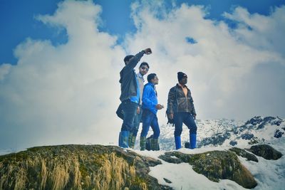 Low angle view of friends standing on snowcapped mountain during winter