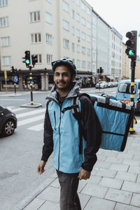 Portrait of smiling delivery man standing on sidewalk in city