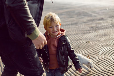 Father and son in leather jackets in autumn walking in nature near the bay on the beach with sand