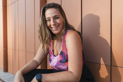 Beautiful smiling woman with brown hair crouching in front of wall