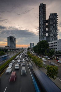 City street by modern buildings against sky during sunset