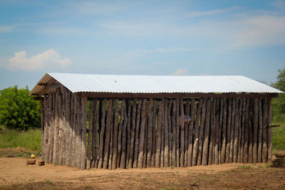 Wooden fence on field by houses against sky