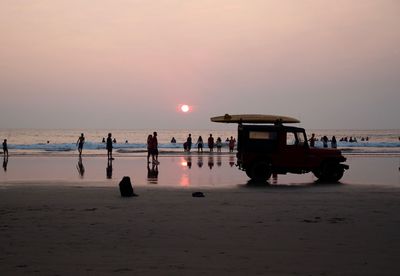 People at beach against sky during sunset