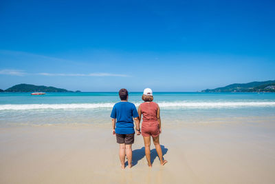 Rear view of couple holding hands at beach against blue sky