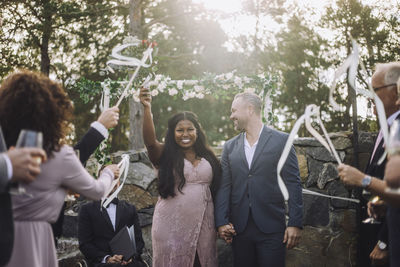 Happy young bride holding hand of groom while walking amidst guests on wedding day