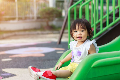 Portrait of cute baby girl sitting on slide at park