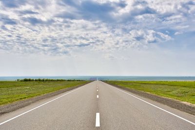 Road passing through field against sky