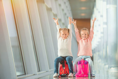 Portrait of cute sisters sitting on luggage at airport