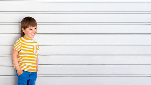 Portrait of smiling boy on white background with stripes. kid stands near light grey wall. 