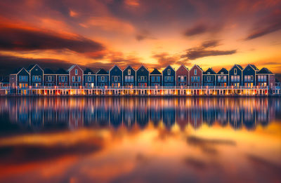 Houses reflecting on calm lake against orange sky during sunset