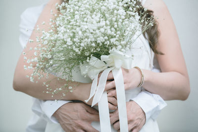 Midsection of woman holding bouquet against white wall