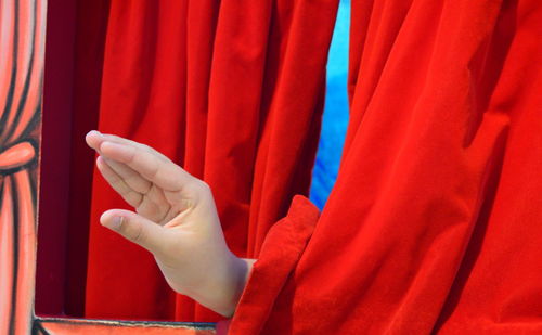 Cropped image of hand gesturing amidst curtains