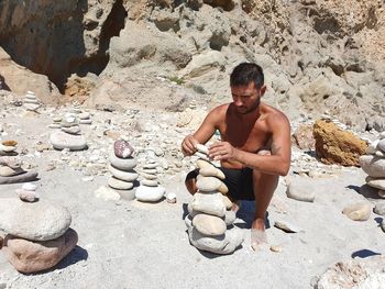 Full length of shirtless man sitting on rock