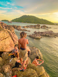 Rear view of shirtless boy on rock by sea against sky