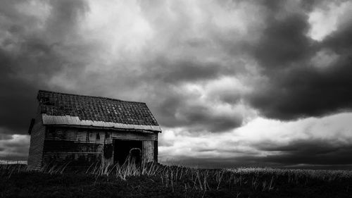 Abandoned building on field against cloudy sky