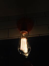 Illuminated light bulb hanging against black background