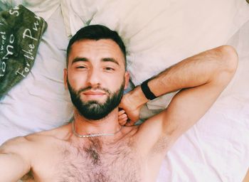 Directly above portrait of shirtless young man lying on bed