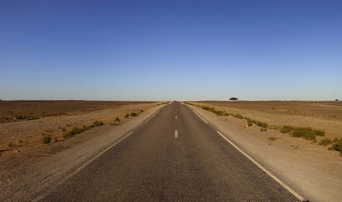 Road leading towards landscape against clear sky