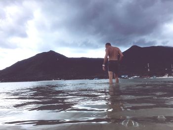 Rear view of shirtless man standing in water