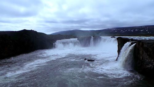 Scenic view of waterfall against cloudy sky