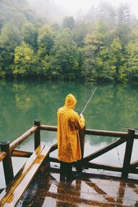 Rear view of woman standing by lake against trees