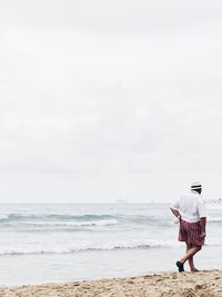 Rear view of man waking at shore against clear sky