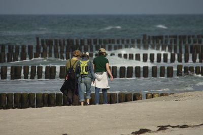 Rear view of people walking at beach against sky