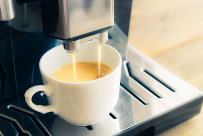 White ceramic cup of fresh espresso with foam in the coffee machine.