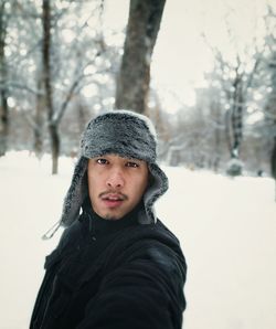 Portrait of man wearing fur hat while standing against bare trees during winter
