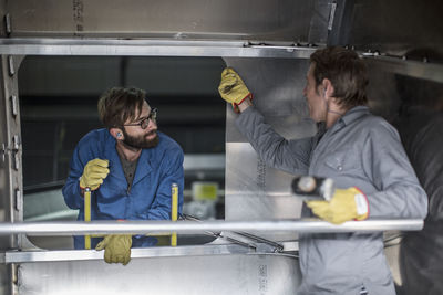 Two men discussing inside of steel container in factory