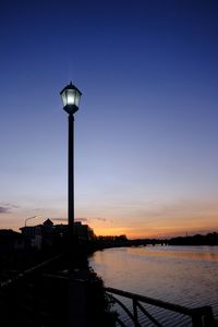 Silhouette street light by river against sky at sunset